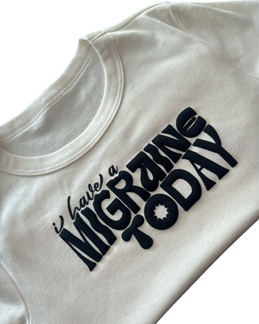 off-white folded crop top tshirt with black text 'I Have a Migraine Today' on a white background