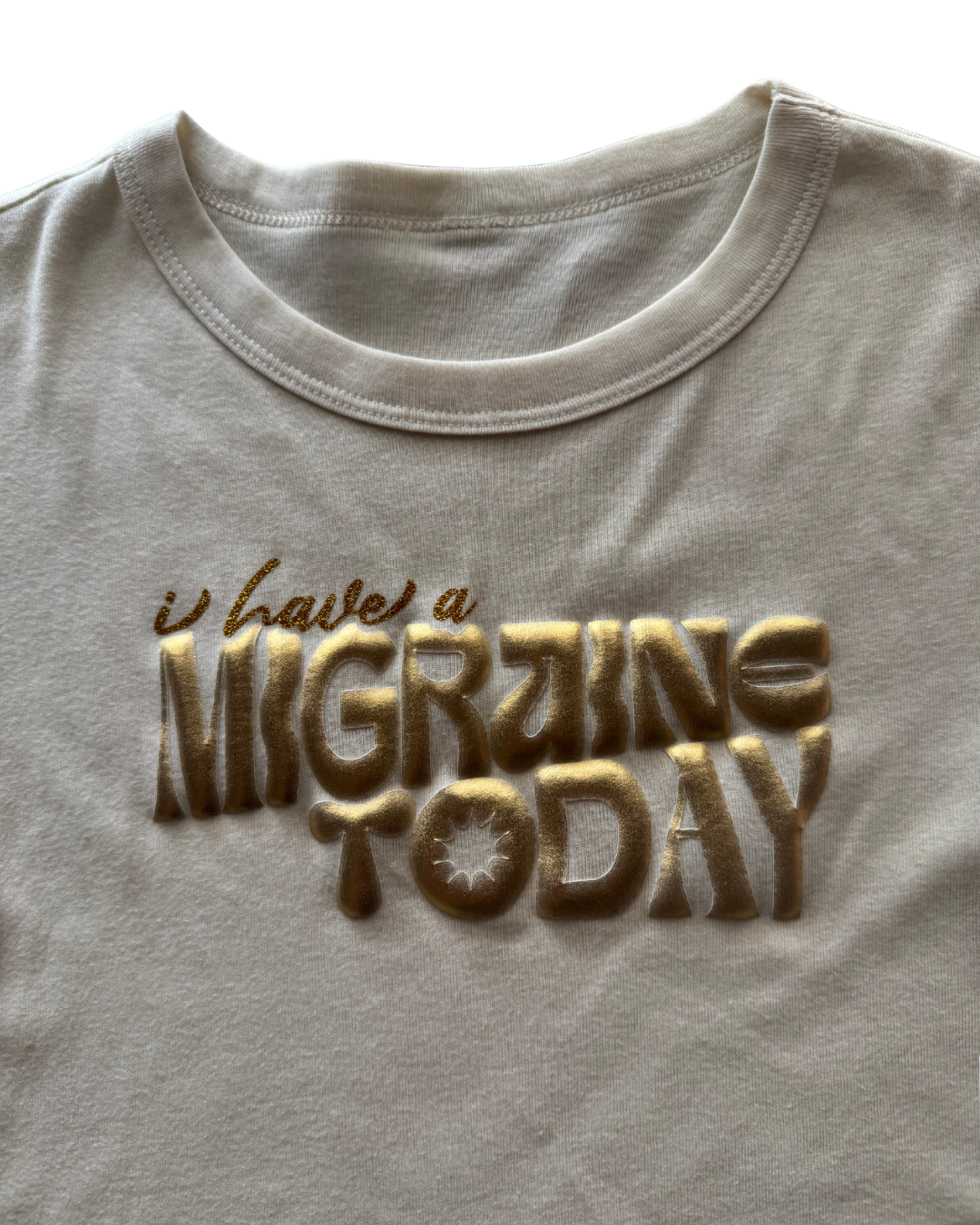 off-white t-shirt with 'I have a MIGRAINE TODAY' text in gold on a white background