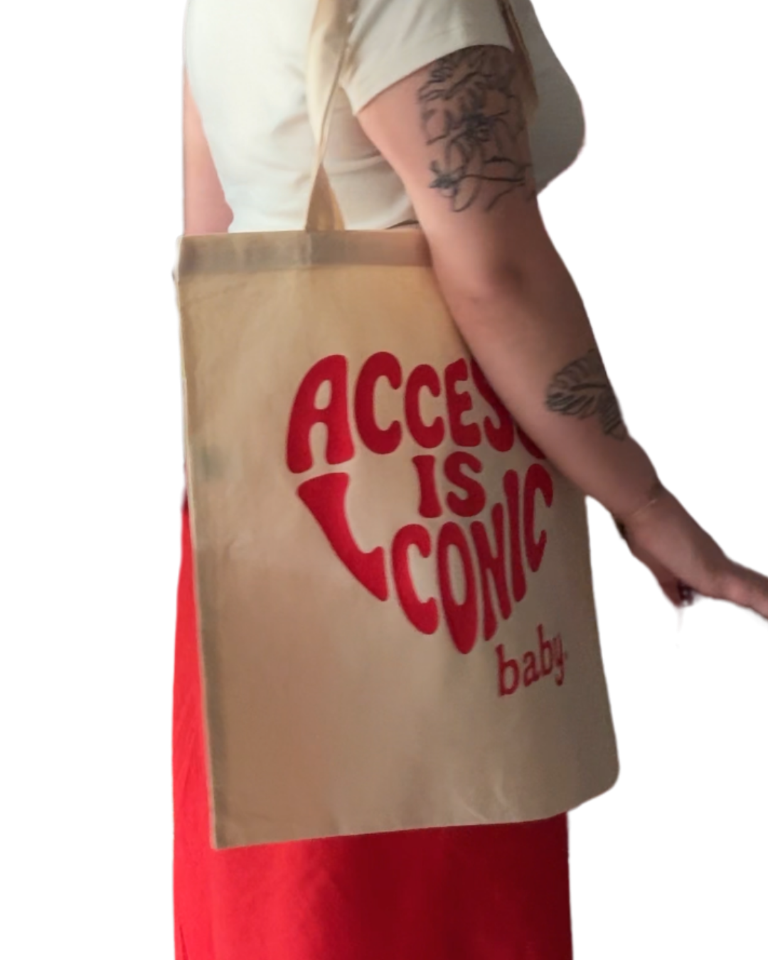 A close up  photo of woman wearing a cotton tote with the "Access Is Iconic Baby" design in red. It's in the center of the tote. 
