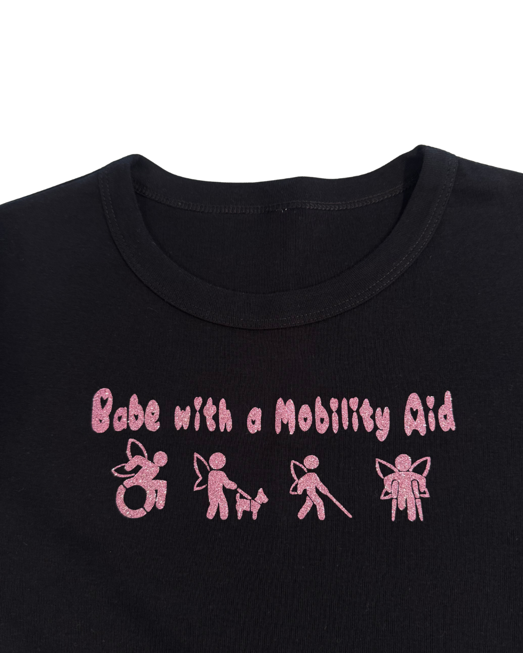 Close up of black t-shirt with pink glitter text that says "Babe with a mobility aid" in bubble letter typography and disability symbols on a white background