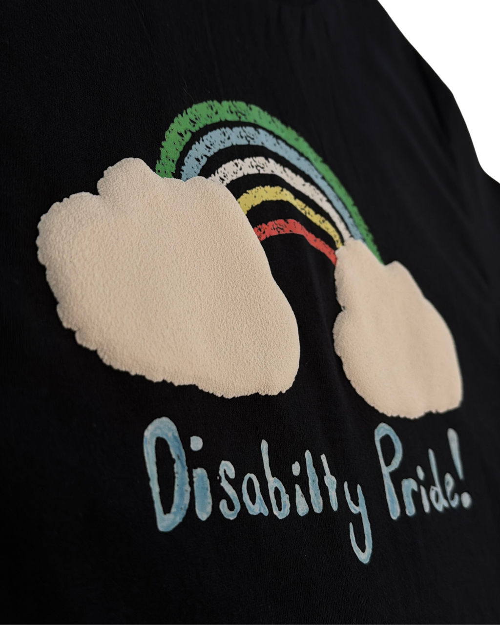 Black shirt with a drawn rainbow and 3D puff textured cloud design, and hand-drawn 'Disability Pride!' text.