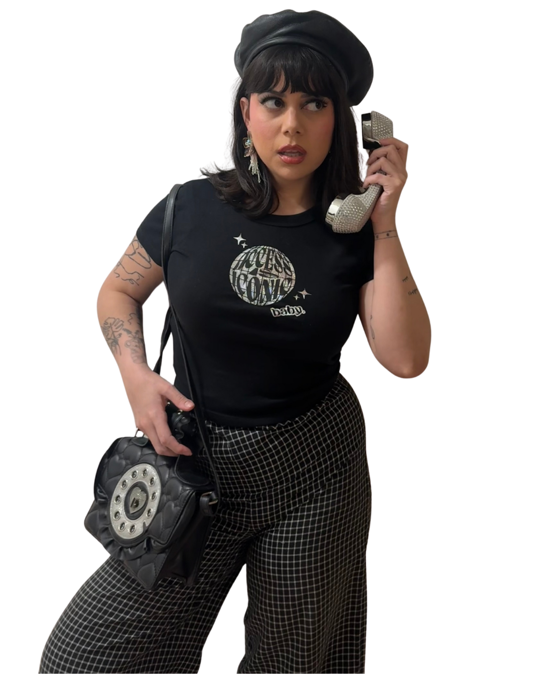 a photo of a woman wearing the black access is iconic baby crop top styled with black grid pattern pants, a telephone shaped purse, a black beret, and silver earrings.