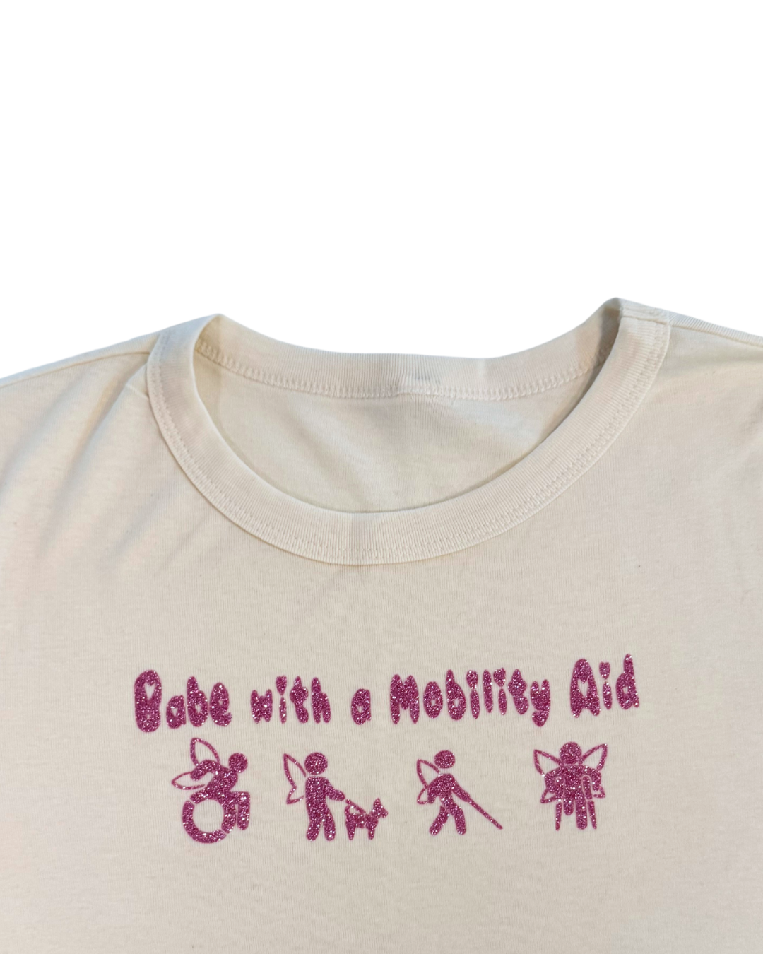 close up of off-white t-shirt with pink glitter text that says "Babe with a mobility aid" in bubble letter typography and disability symbols on a white background
