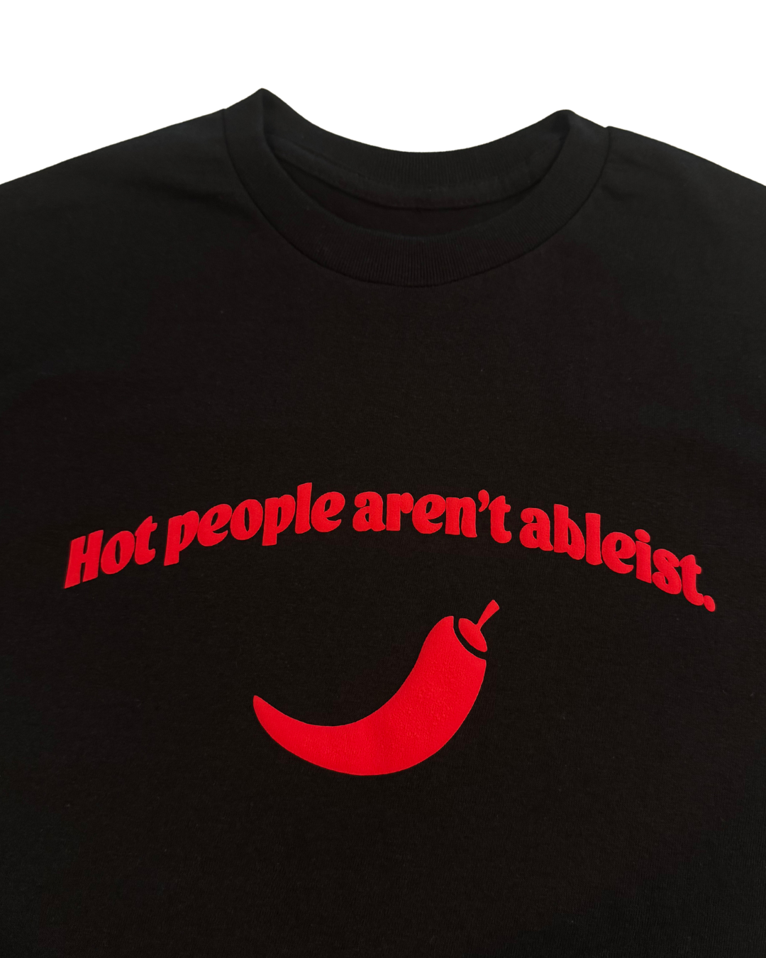close up black regular length tshirt with red text and a red pepper graphic that says "hot people arent ableist" on a white background. Gender neutral version