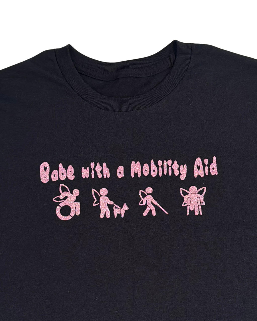 close up of back t-shirt with pink glitter text that says "Babe with a mobility aid" in bubble letter typography and disability symbols on a white background