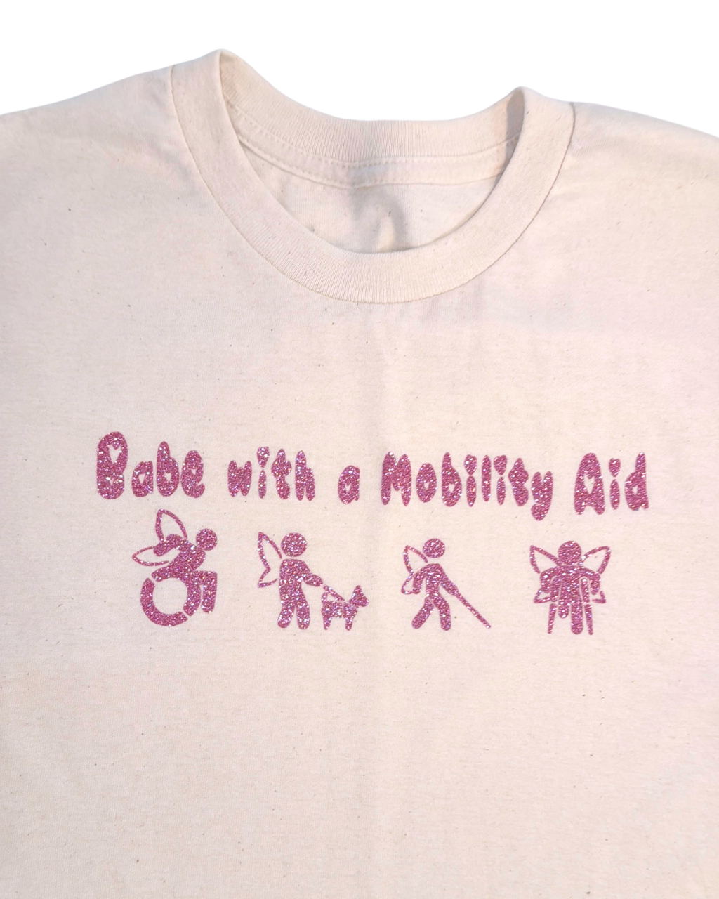 close up of off-white t-shirt with pink glitter text that says "Babe with a mobility aid" in bubble letter typography and disability symbols on a white background