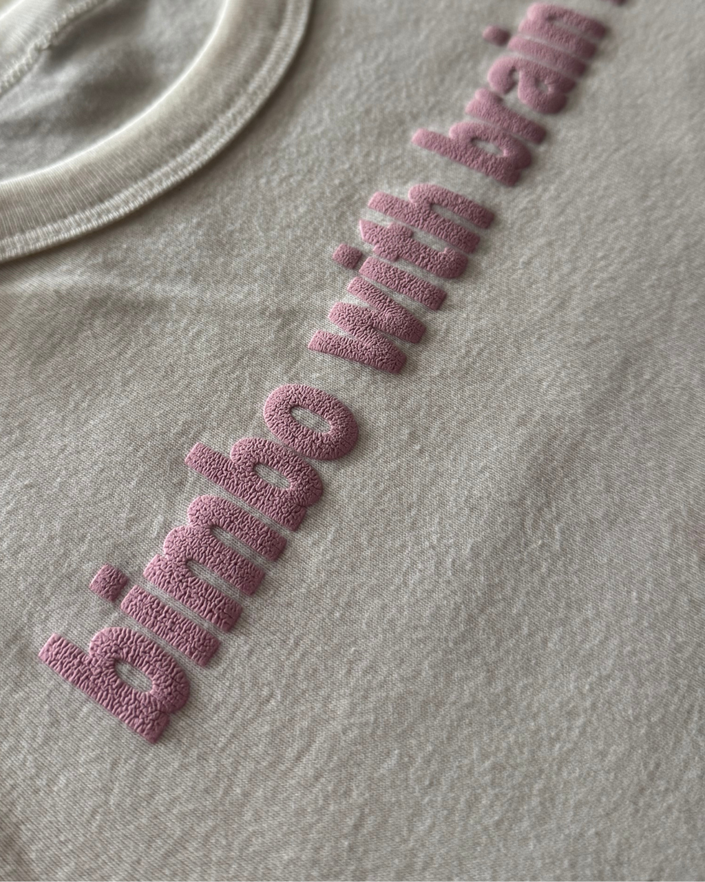 white t-shirt with a textured pink logo on a gray background