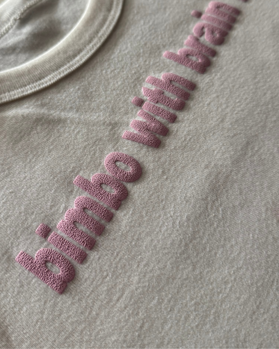 white t-shirt with a textured pink logo on a gray background